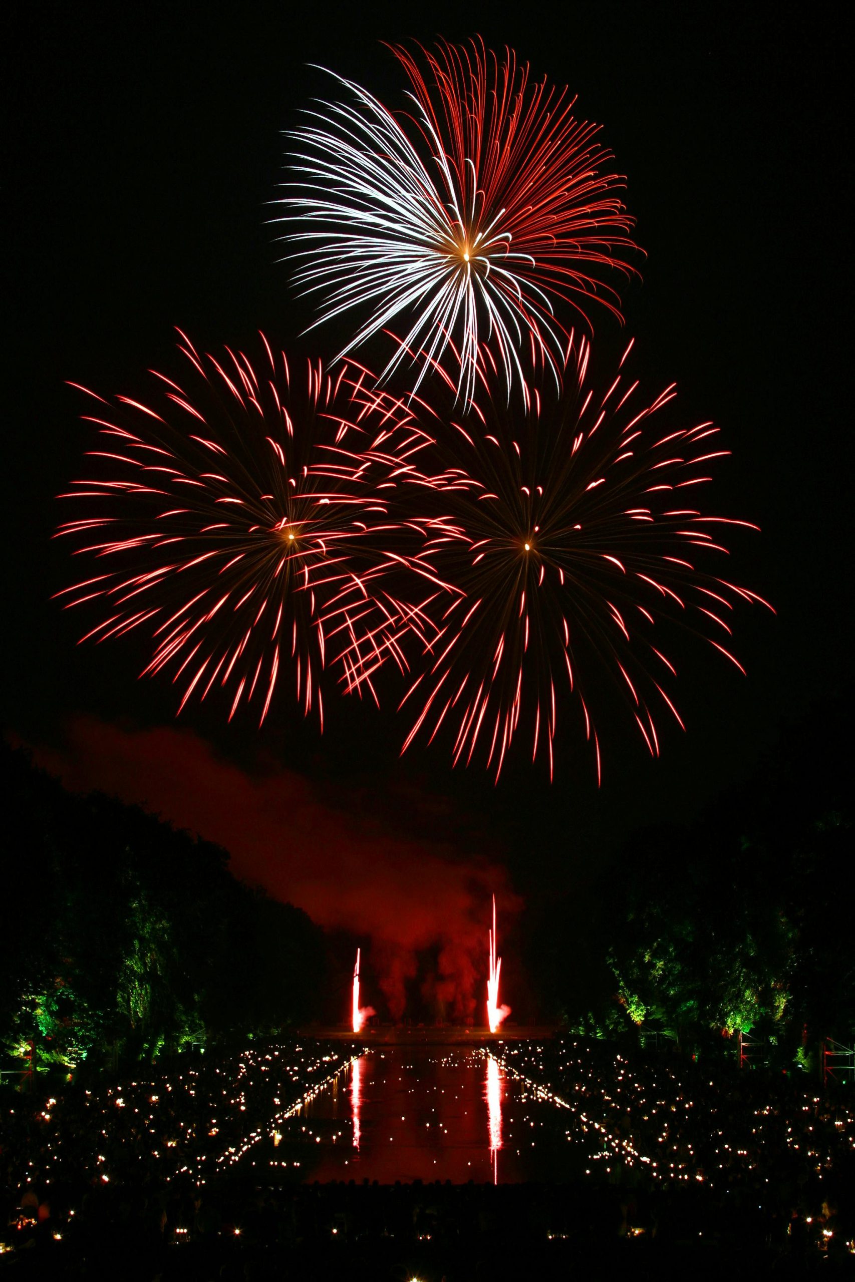Vibrant fireworks illuminate the night sky over a reflective water surface, creating a festive atmosphere.